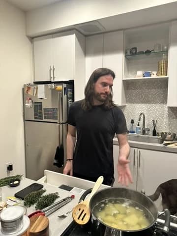 Isaac in his kitchen mid-conversation, with a pot of potatoes boiling and fresh herbs on the counter